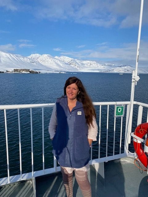 Mari Jungstedt på en båt på Svalbard med hav och snötäckta fjäll bakom sig.