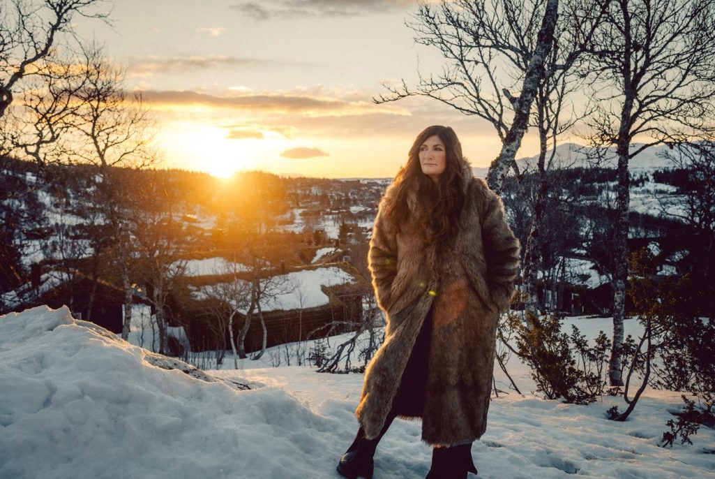 Mari Jungstedt står i ett snötäckt fjällandskap i solnedgång.
