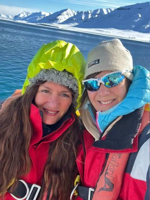 Mari Jungstedt och Alexandra Zazzi på båt med snötäckta fjäll i bakgrunden på Svalbard.